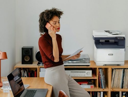 Een vrouw die aan een bureau zit en belt naast een Xerox® C325-printer