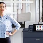 Een vrouw staat naast de Xerox® PrimeLink® C9200 Serie Printer in een moderne kantooromgeving