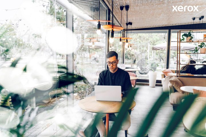 Een man die ijverig op zijn laptop werkt in een bruisend café, verzonken in zijn taken te midden van een levendige omgeving.