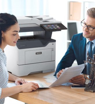 Een man en een vrouw zitten aan een tafel, in gesprek terwijl er een Xerox®-printer in de buurt staat.