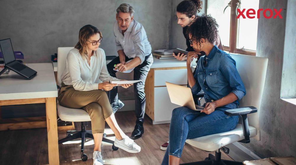 Vier collega's werken samen in een modern kantoor.